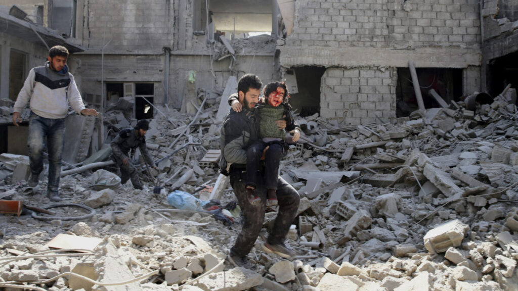 Un hombre carga a un niño herido sobre los escombros de Guta. Fotografía: Bassam Khabieh.